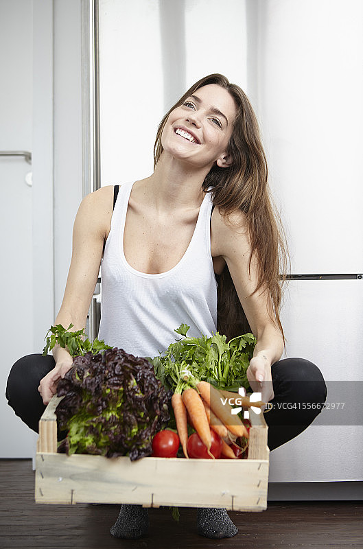 在厨房里拿着装满新鲜蔬菜的板条箱的快乐年轻女人图片素材