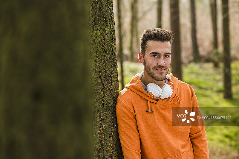年轻男子戴着耳机在森林里微笑图片素材