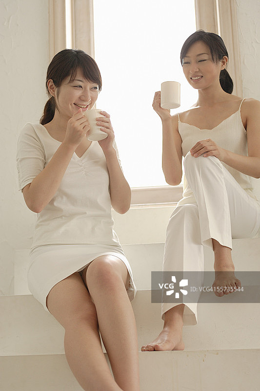 两位年轻女性拿着咖啡杯坐着图片素材