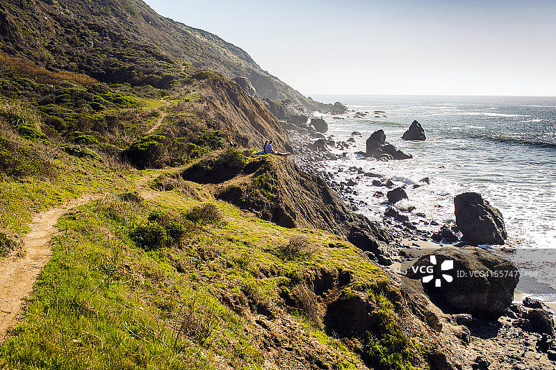 坐在靠近海洋的岩石海岸线小路上的人们图片素材