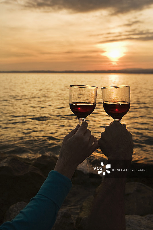 一对情侣在湖边日落时举起酒杯图片素材