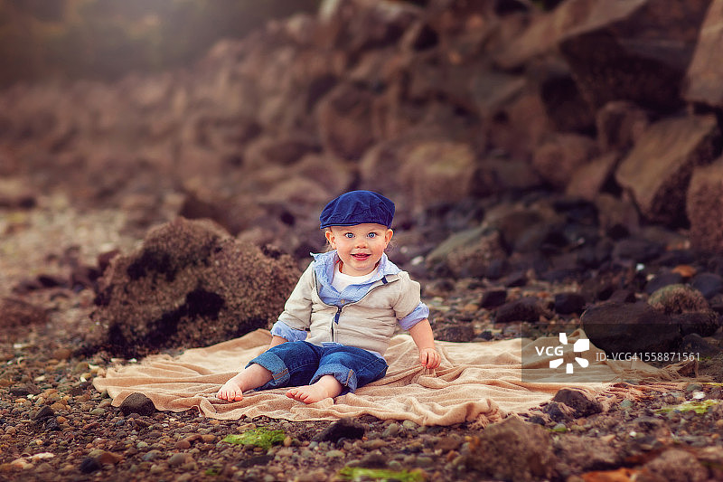 小男孩坐在岩石海滩的毯子上图片素材