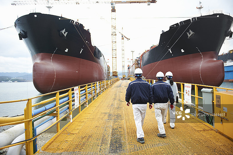 三名走向港口船只的工人背影，韩国高城郡图片素材