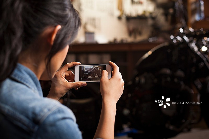 在车间，女机械师用智能手机拍摄摩托车图片素材