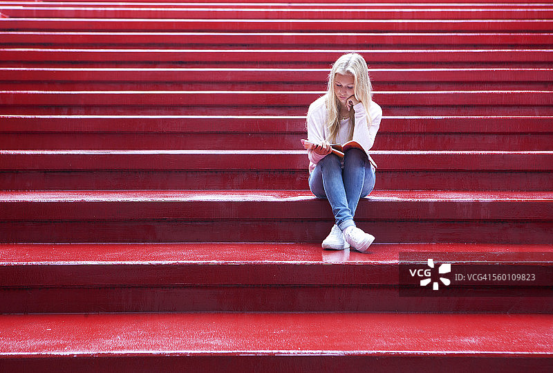 坐在红色楼梯上阅读的少女图片素材