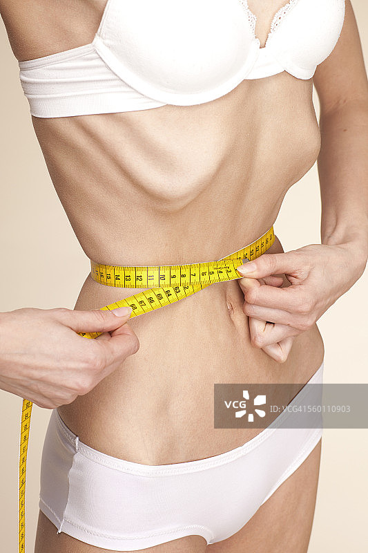 测量腰围的厌食症年轻女人图片素材
