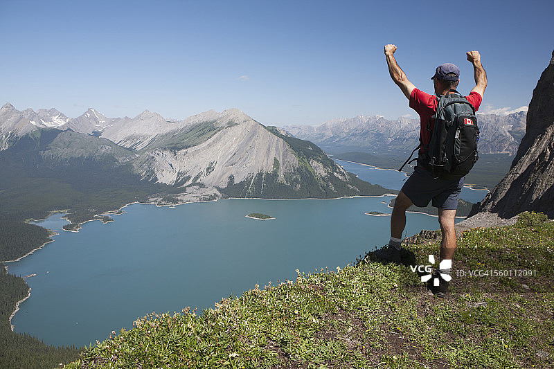 徒步男人站在山脊上俯瞰翠绿的湖泊和山脉图片素材