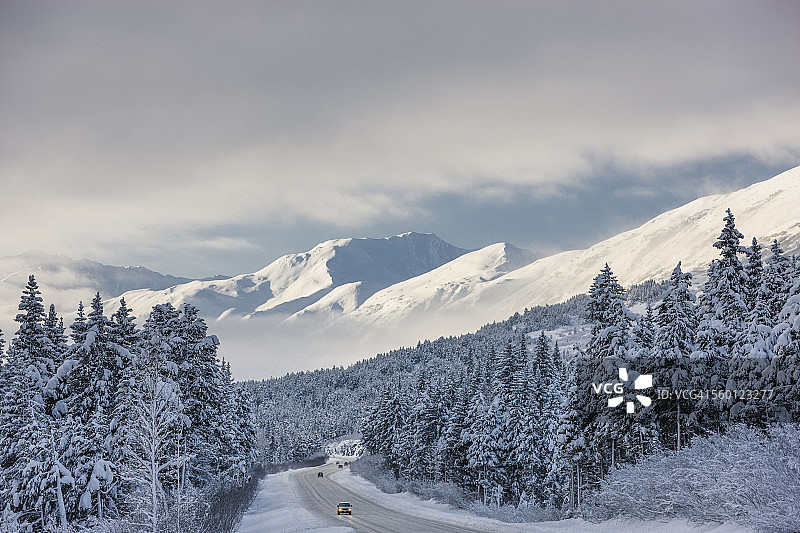 冬季暴风雪后,楚加奇国家森林公园特纳根隘口上方的克奈山脉,苏厄德高速公路上的云层消散,树木上覆盖着新鲜的雪,清晨的阳光图片素材