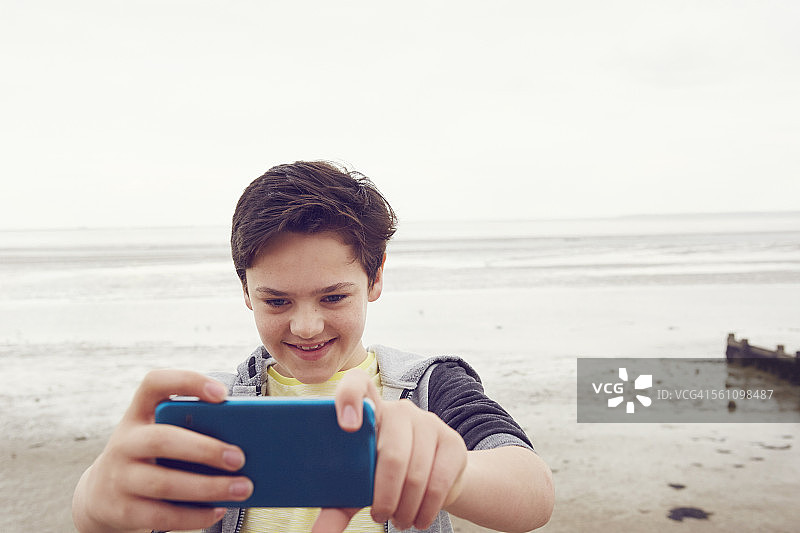 英国埃塞克斯滨海绍森德海边，微笑少年用智能手机自拍图片素材