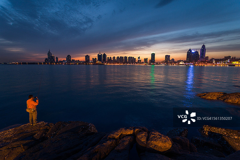 夜晚在中国青岛湾旁钓鱼的男人图片素材