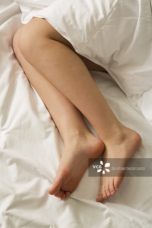 白色床上女性裸腿的高角度视图图片素材