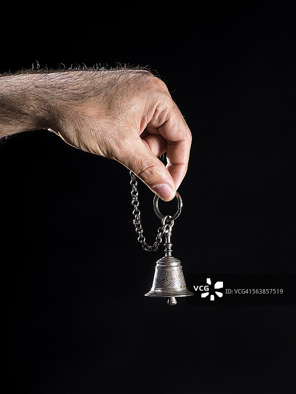 黑色背景上手持银色铃铛图片素材