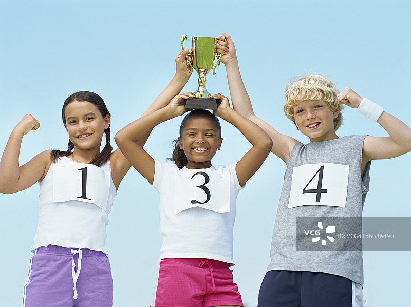 两个女孩和一个男孩举起奖杯的低角度视图图片素材