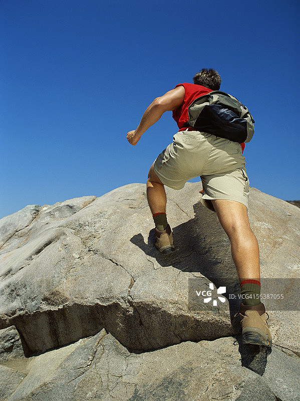 仰视：一名年轻男子攀爬岩石图片素材