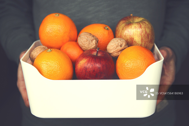 男人手捧苹果橘子核桃碗特写图片素材