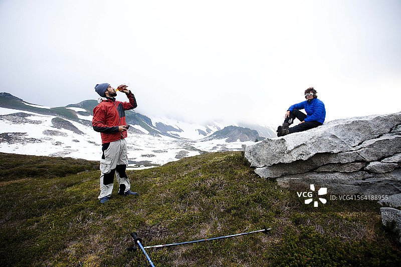 两名登山者在攀登顶峰前休息，享用波本酒图片素材