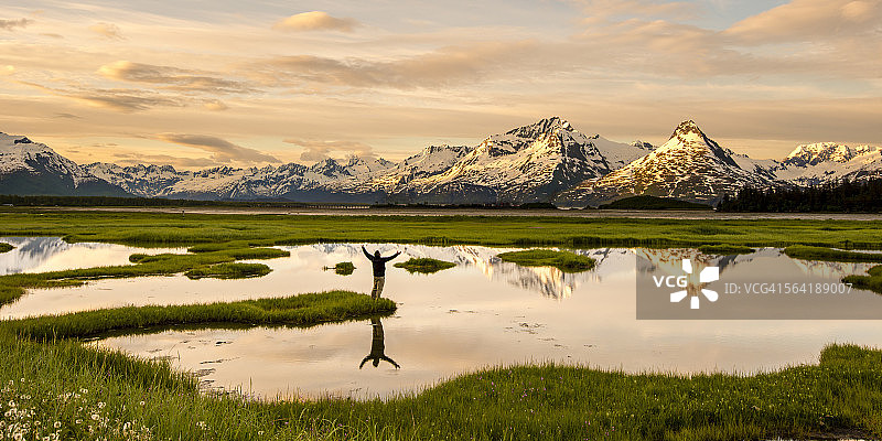 男人站在池塘边远眺山脉，美国阿拉斯加州瓦尔迪兹图片素材