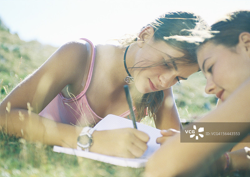 两个女孩躺在草地上，一个在写作图片素材