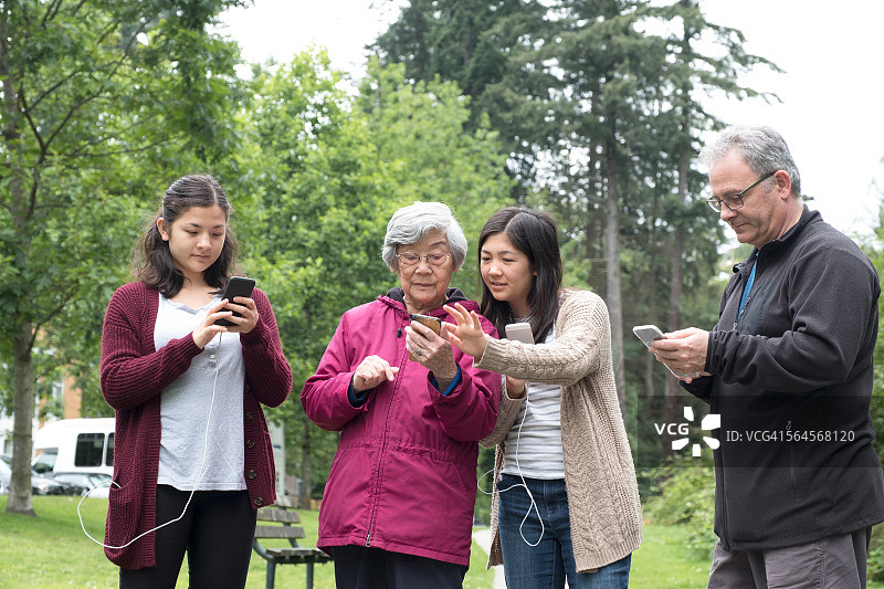 在公园里玩智能手机增强现实游戏的多代混合家庭图片素材