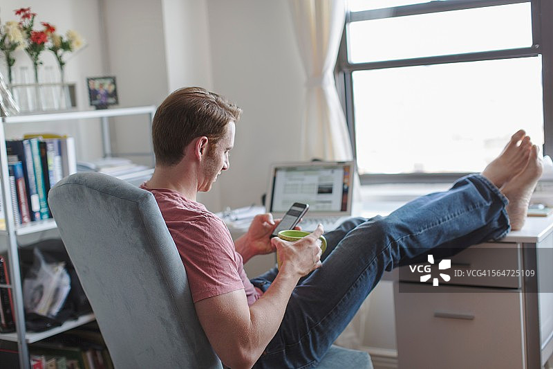 脚放在桌子上阅读智能手机短信的中年男人图片素材