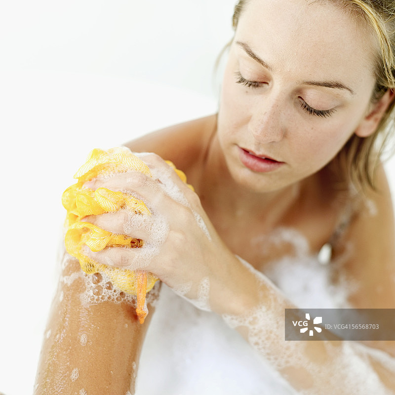 年轻女子在泡泡浴中用丝瓜瓤擦洗身体特写图片素材