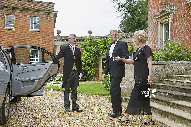 在豪宅外为一对夫妇打开车门的白人管家图片素材