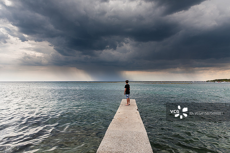 男孩站在防波堤上看暴风雨图片素材