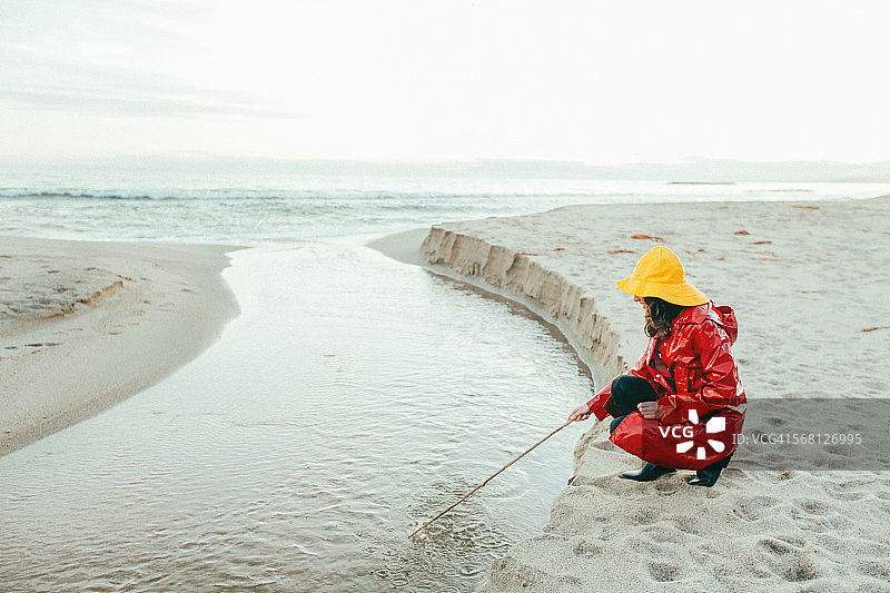 穿雨衣的女人在海滩上拿着棍子图片素材