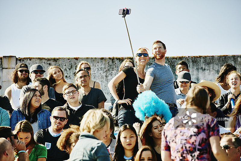 在体育场人群中使用自拍杆的情侣图片素材