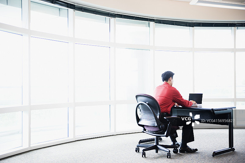 坐在桌旁用电脑工作的商人的背影图片素材