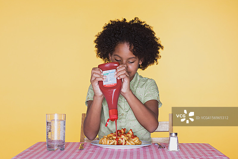 在卷曲薯条上挤番茄酱的女孩图片素材