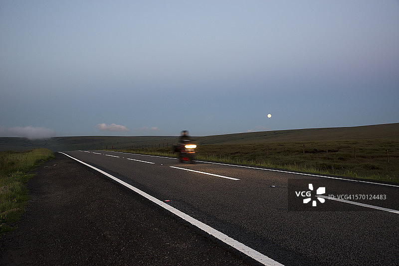在偏僻的道路上的摩托车，月亮在山上升起图片素材