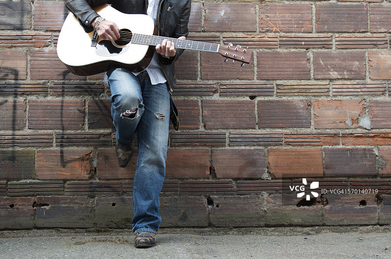 在小巷里弹吉他的皮夹克牛仔靴男人图片素材