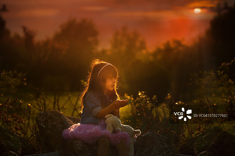 夕阳下抱着玩具的漂亮女孩图片素材