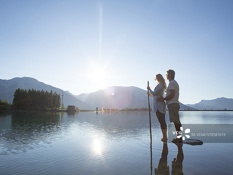 情侣在岩石岛上小憩，欣赏山间湖泊图片素材
