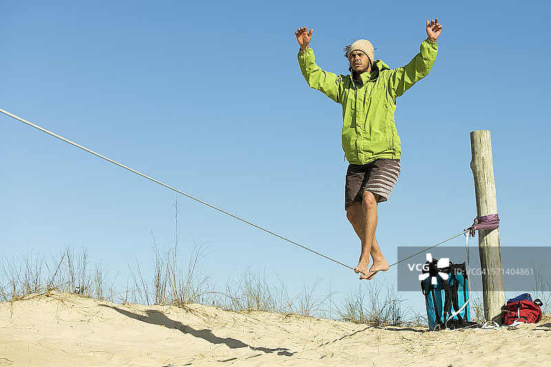 男子在白色沙滩上走软绳图片素材