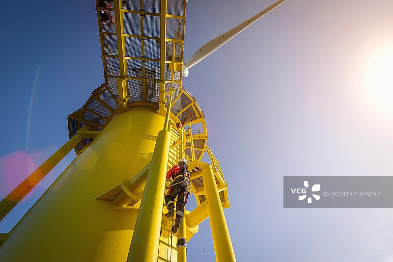 工程师从船上爬上海上风力发电机的风力涡轮机，低角度视图图片素材