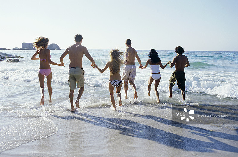 一群手牵着手在海滩上奔跑的人的背影图片素材