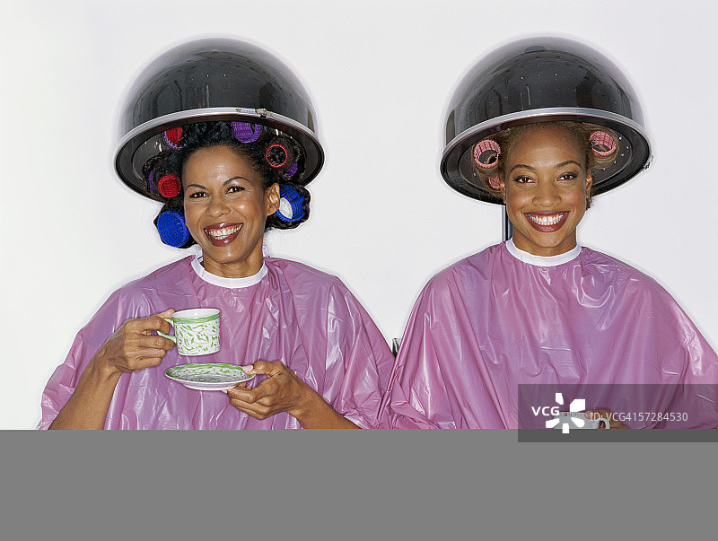 两位年轻女性在美容院，坐在吹风机下图片素材