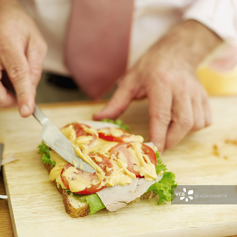 年轻男人在火腿三明治上涂奶酪酱特写图片素材
