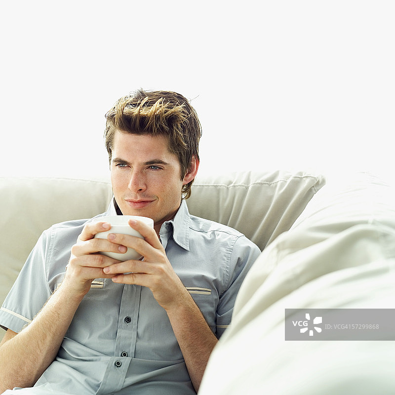 年轻男人坐在沙发上喝咖啡图片素材