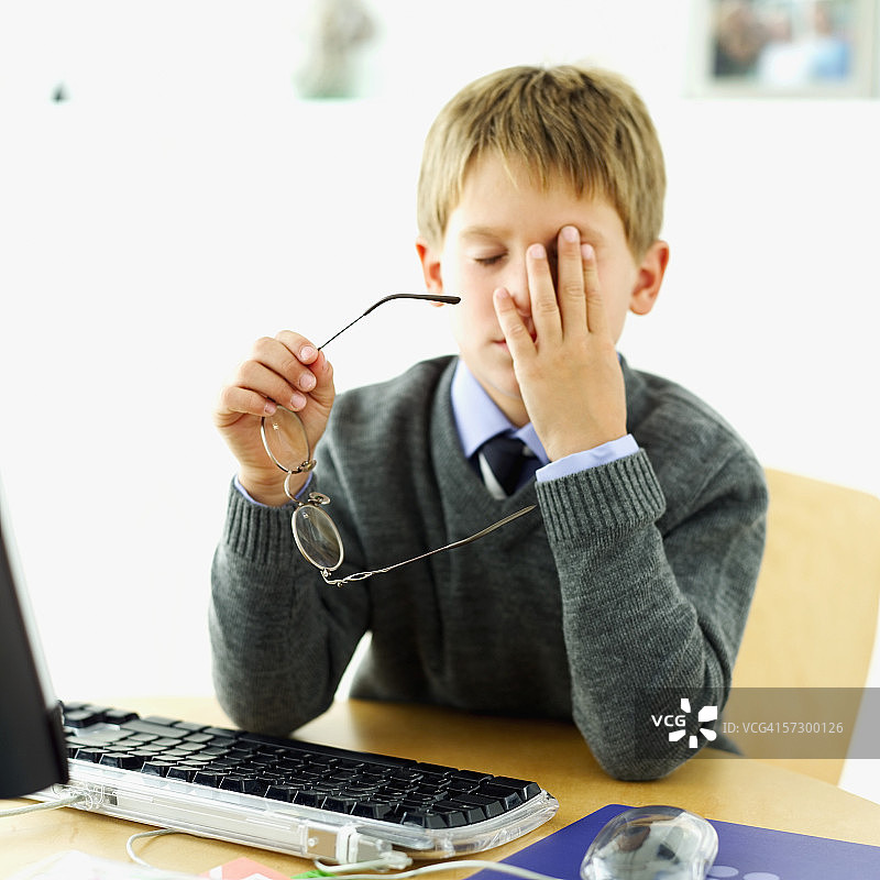 男孩在电脑桌旁揉眼睛的特写图片素材