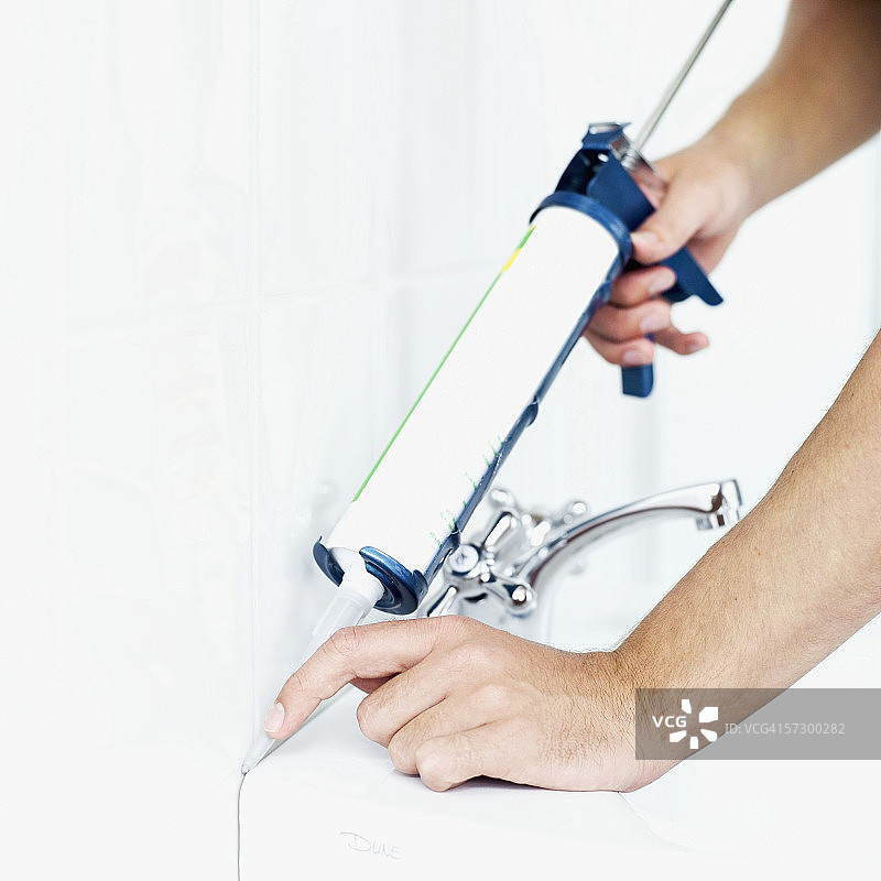 男人在洗手盆和瓷砖墙之间使用填缝枪特写图片素材