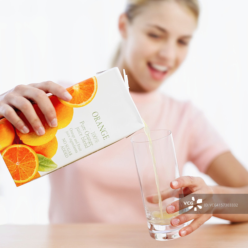 年轻女子将纸盒果汁倒入玻璃杯中特写（模糊）图片素材