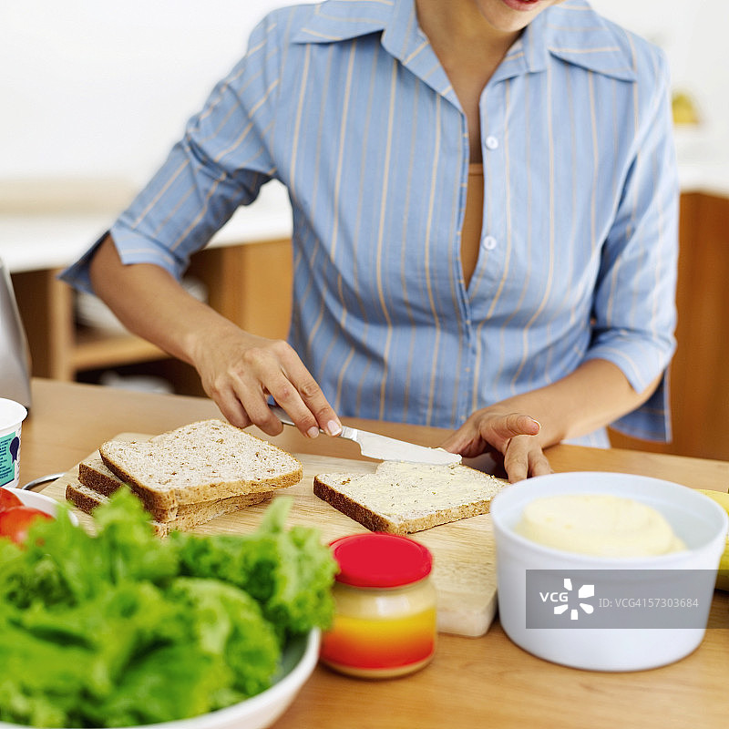 年轻女人往一片棕色面包上涂黄油图片素材