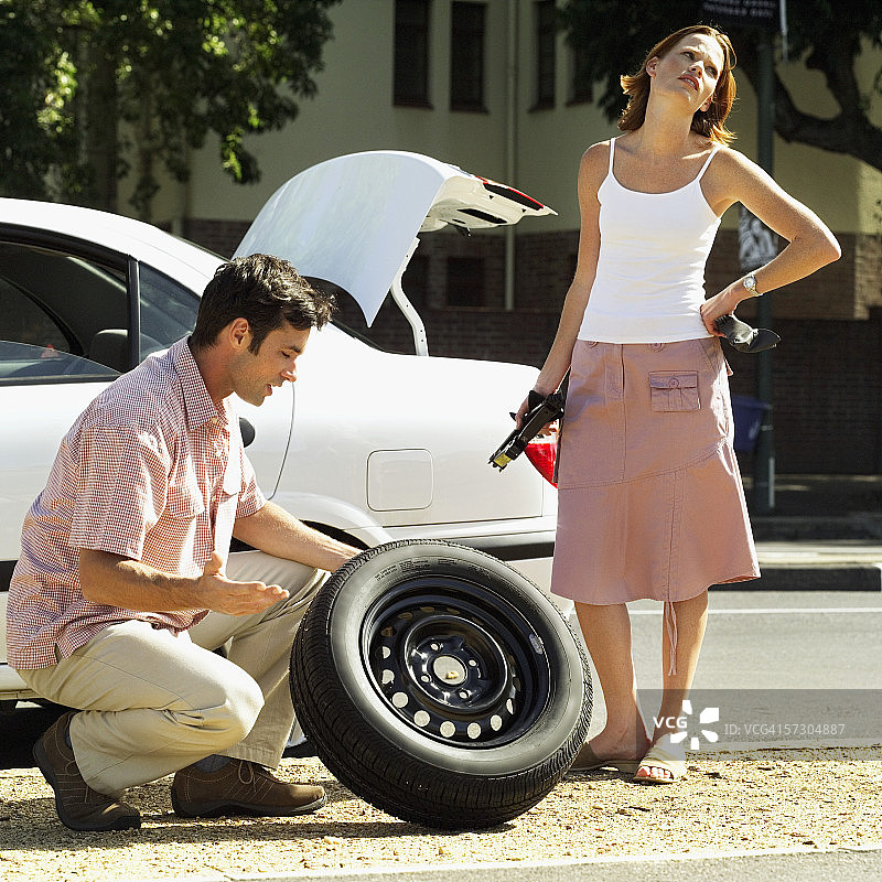 年轻男子拿着备用轮胎，年轻女子拿着千斤顶站立图片素材