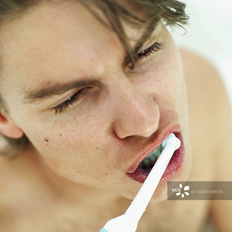 一位年轻男子用电动牙刷刷牙的特写图片素材