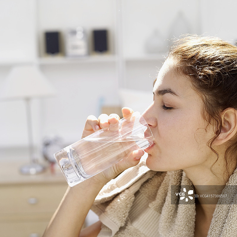 年轻女人用玻璃杯喝水，脖子上围着毛巾图片素材