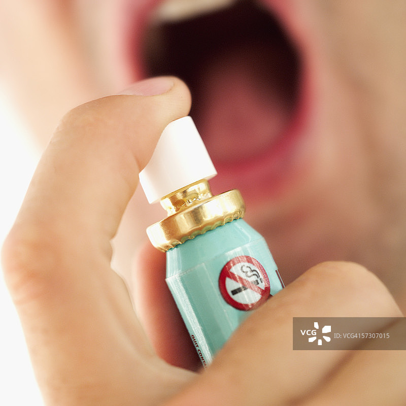 人手拿着喷雾器对着嘴的特写。图片素材