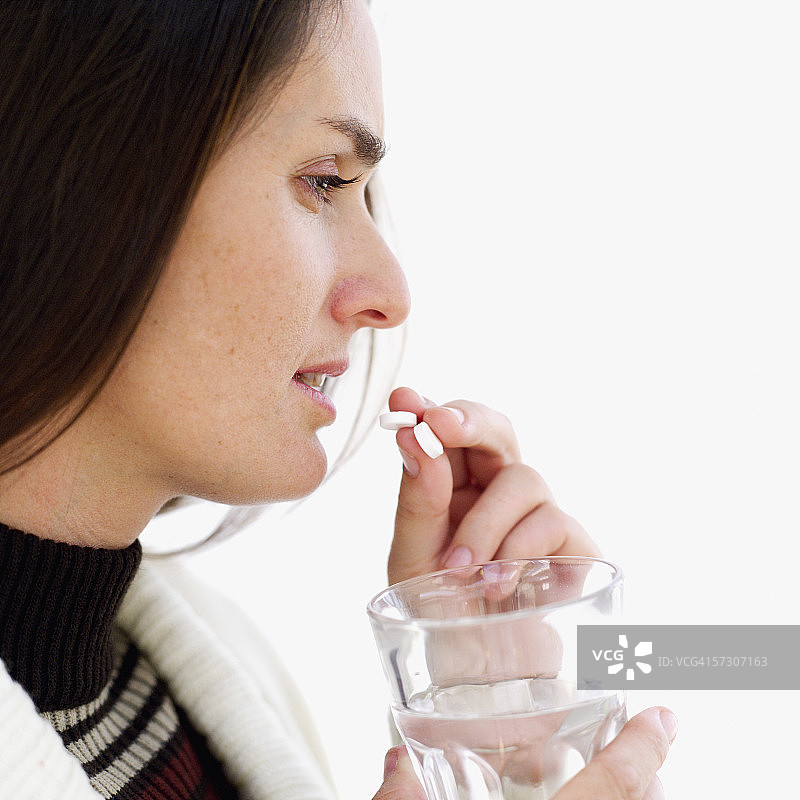 吃药并拿着一杯水的年轻女人的侧面轮廓图片素材